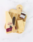 Wooden cutting board with cheese, a knife, and a jar of jam on a white surface