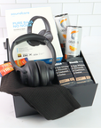 Black headphones with packaging, Celsius drinks, and protein bars in a box on a white tiled background